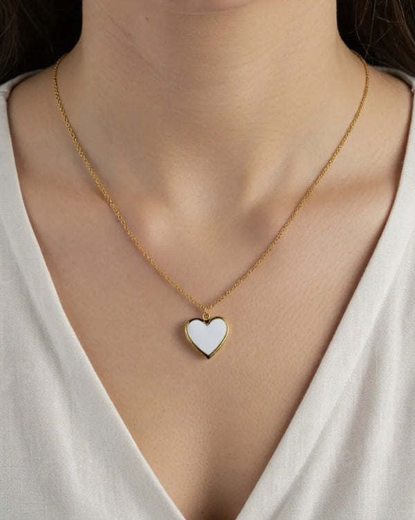 Gold necklace with a heart-shaped pendant worn by a person in a white top.